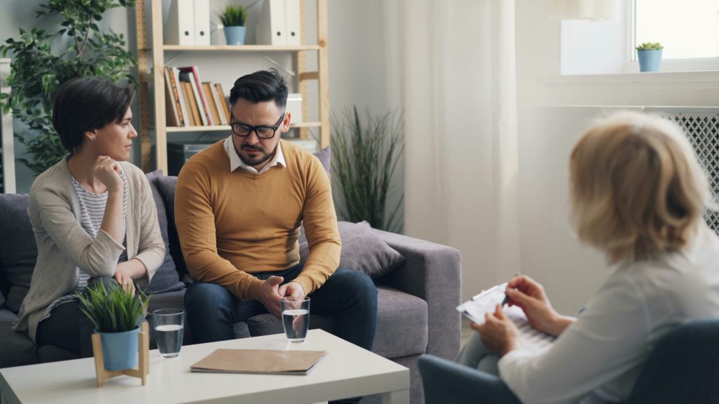 couple assis sur un canapé face à une dame qui prend des notes